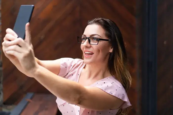 Woman using smartphone to virtually try on eyeglasses with augmented reality technology.