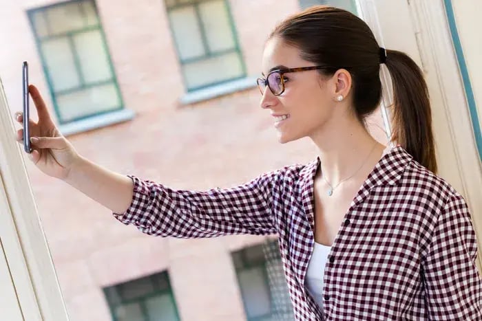 Woman using smartphone to test eyeglass frames virtually with augmented reality try-on.