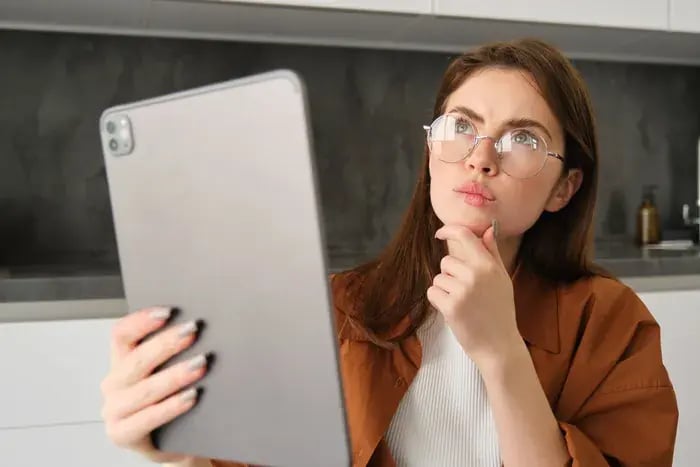 Woman evaluating different eyeglass frames on tablet using virtual try-on application.